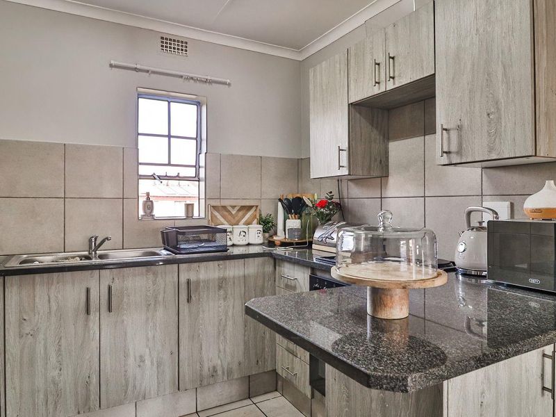 A functional kitchen featuring wood-look laminate cabinetry, granite countertops, a tiled backsplash, and integrated appliances including an oven and hob.