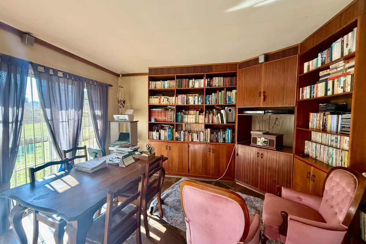 A study or living area featuring extensive built-in wooden cabinetry and shelving, large windows with natural light, and tiled flooring.