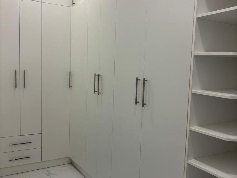 A modern walk-in closet or dressing area featuring extensive white built-in cabinetry, open shelving, and polished marble-look floor tiles.