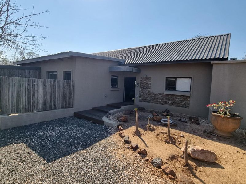 Front elevation of a modern house featuring a corrugated metal roof, stone cladding accents, and a timber entrance deck with a gravel driveway.