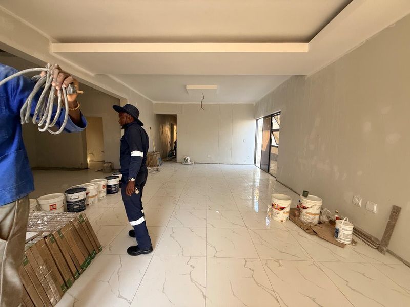 Spacious living area currently under renovation, featuring large format marble-look porcelain tiles, recessed ceiling details, and sliding glass doors.
