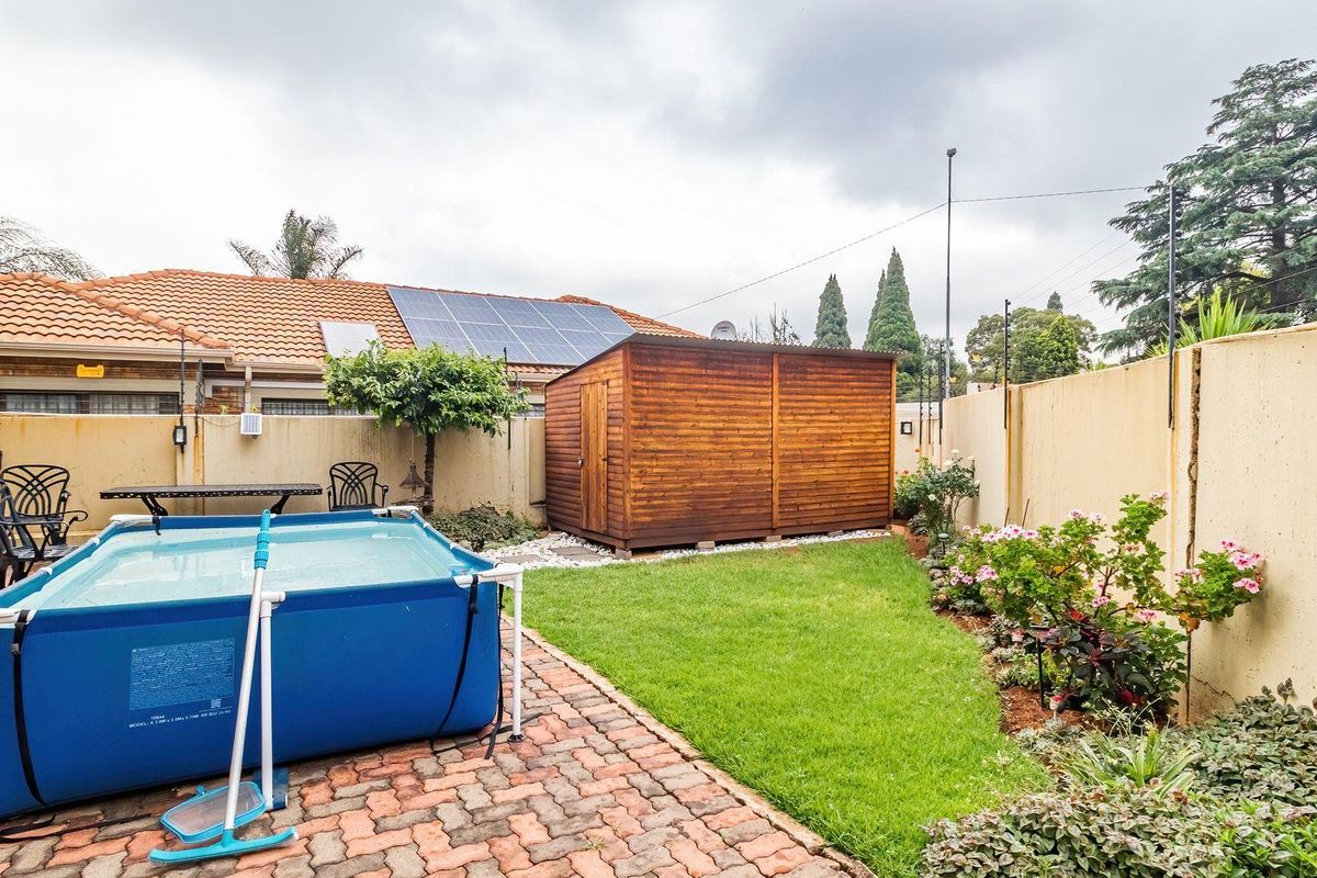 A private rear garden featuring a paved patio area, a small lawn, established garden beds, and a wooden storage shed.