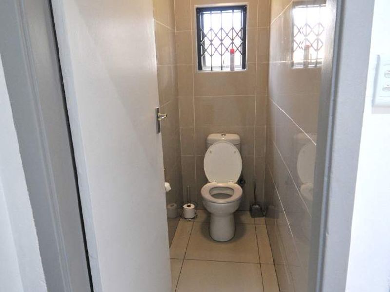A clean and compact guest bathroom featuring floor-to-ceiling tiling, a modern toilet, and a secure window.