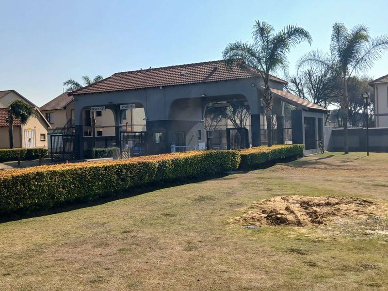 View of the apartment complex security gatehouse entrance with surrounding landscaped hedges and lawn area.