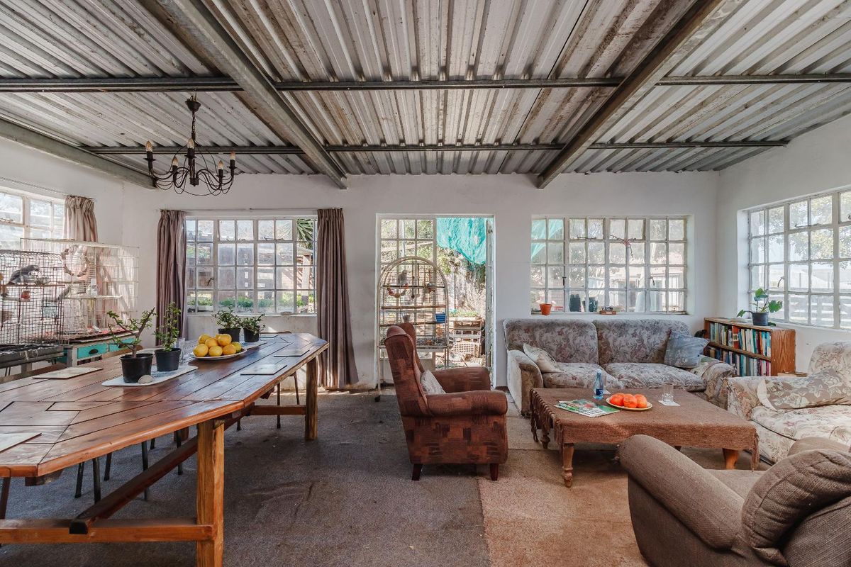 Spacious open-plan living and dining area featuring exposed corrugated metal ceilings and large steel-framed windows providing ample natural light.