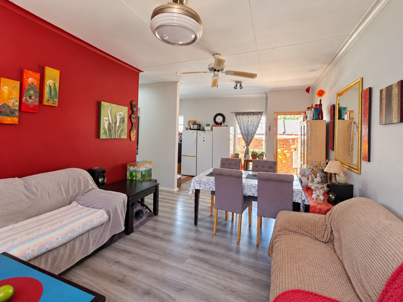 Open-plan living and dining area featuring laminate flooring, a ceiling fan, and a bold red accent wall, providing a functional and connected living space.