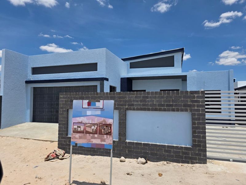 Modern single-story house featuring a blue textured facade, double garage, and a contemporary brick boundary wall with a metal gate.