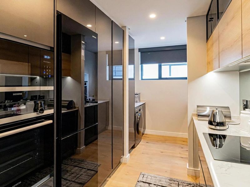 Modern kitchen featuring high-gloss cabinetry, integrated Siemens appliances, stone countertops, and induction hob, finished with light wood-look flooring and recessed lighting.