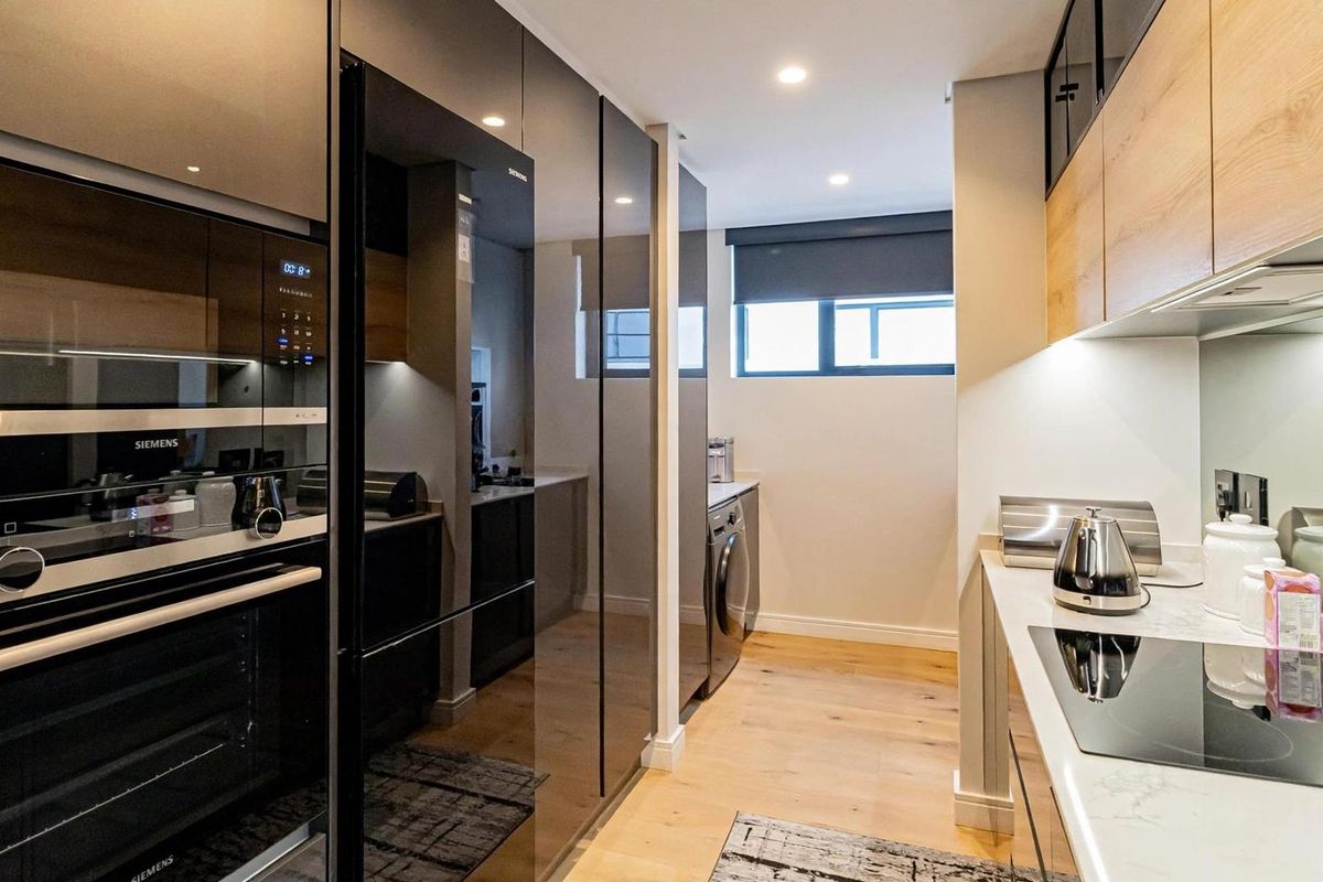 Modern kitchen featuring high-gloss cabinetry, integrated Siemens appliances, stone countertops, and induction hob, finished with light wood-look flooring and recessed lighting.