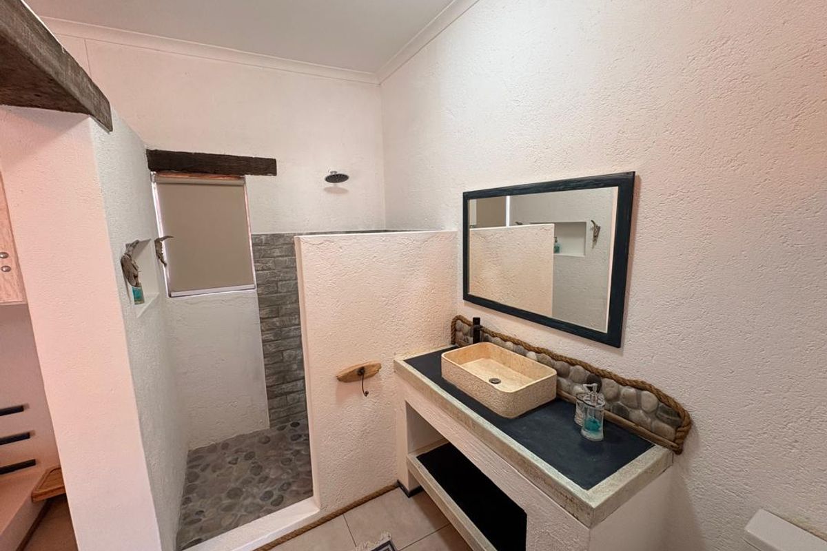 A modern bathroom featuring a walk-in shower with pebble flooring, a unique stone vessel sink, and a custom vanity with a rustic aesthetic.