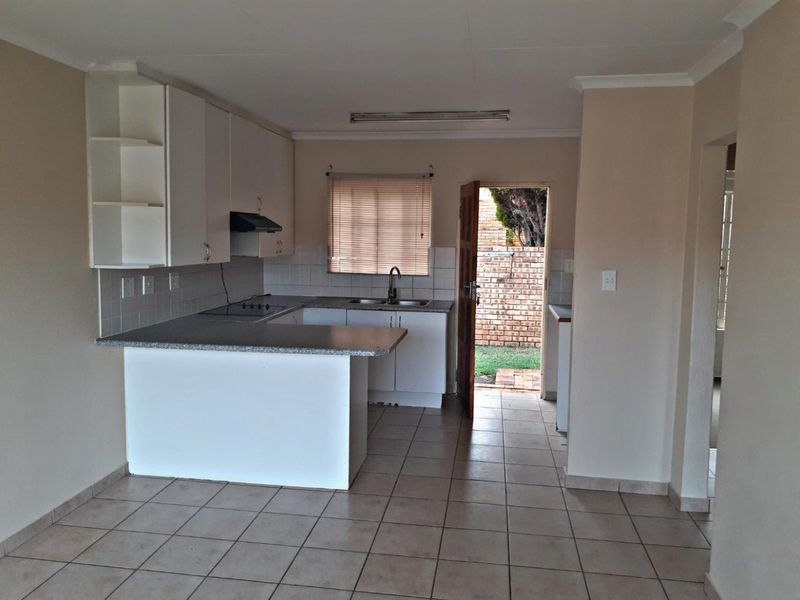 A functional kitchen featuring built-in cabinetry, laminate countertops, and tiled flooring, with direct access to the rear exterior area.