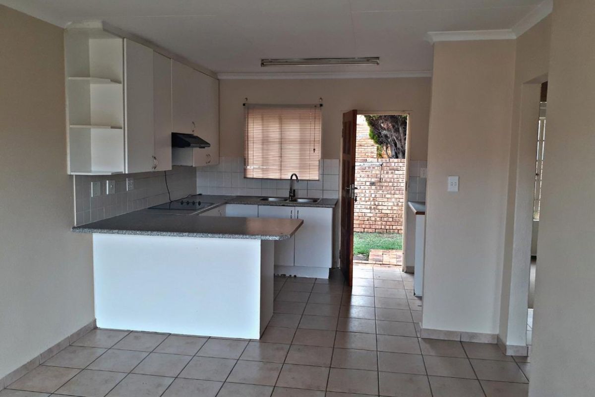 A functional kitchen featuring built-in cabinetry, laminate countertops, and tiled flooring, with direct access to the rear exterior area.