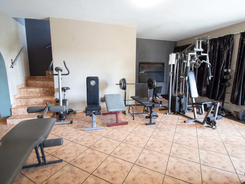 A dedicated home gym space featuring tiled flooring, a staircase with a handrail, and a recessed wall niche.
