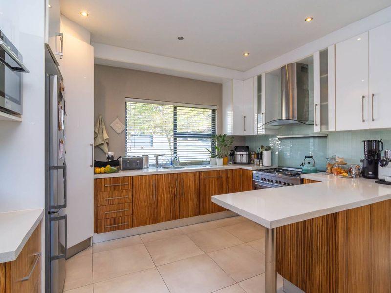 Modern kitchen featuring wood-grain lower cabinetry, white upper cabinets, stone countertops, gas cooktop, and integrated appliances with a clean, contemporary finish.