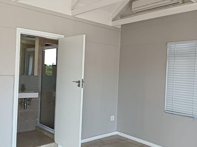 A bright, empty bedroom featuring vaulted ceilings with exposed rafters, tiled flooring, a split-system air conditioner, and an attached en-suite bathroom.
