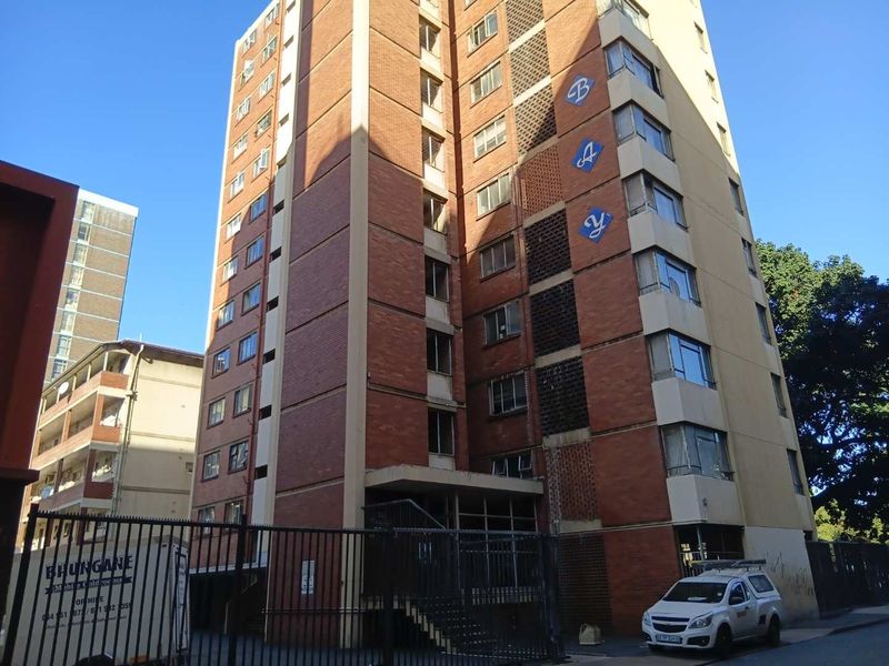 Exterior view of a multi-story brick apartment building featuring a secure gated entrance and functional architectural design.