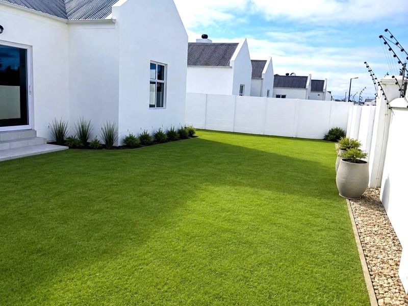A well-maintained rear garden featuring a manicured lawn, paved patio area, and secure perimeter wall with electric fencing.