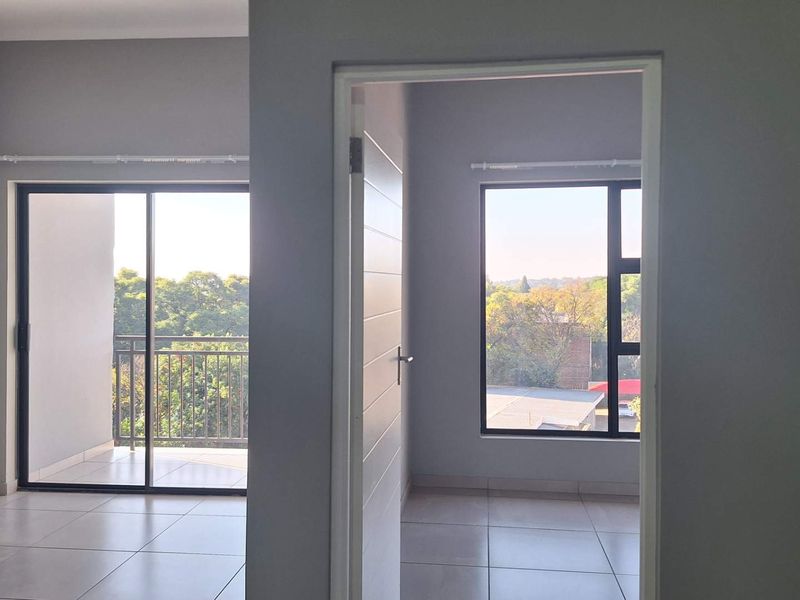 Bright and spacious living area featuring neutral tiled flooring, large aluminium-framed windows, and direct access to a private balcony with scenic views.