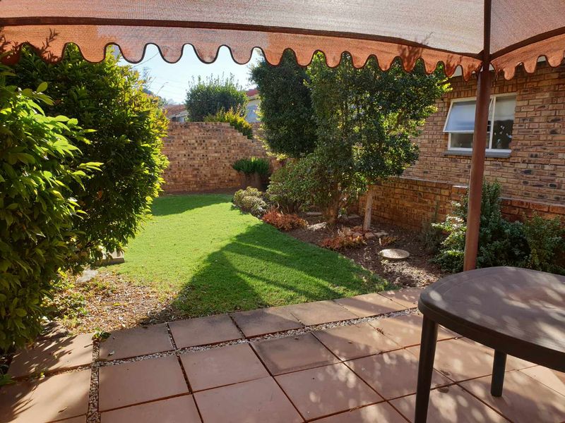 A covered patio area featuring tiled flooring and a shade cloth awning, overlooking a well-maintained private garden with brick boundary walls.