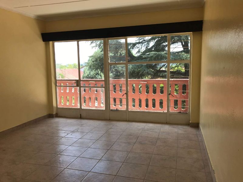 An empty living room featuring tiled flooring and large steel-framed windows providing natural light and access to an outdoor balcony area.