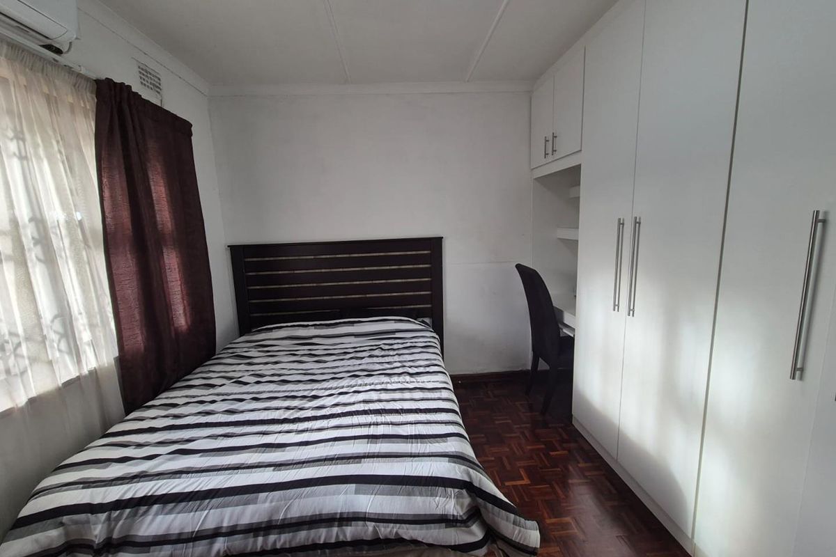 A functional bedroom featuring parquet flooring, built-in white cabinetry with an integrated desk space, and a wall-mounted air conditioning unit.