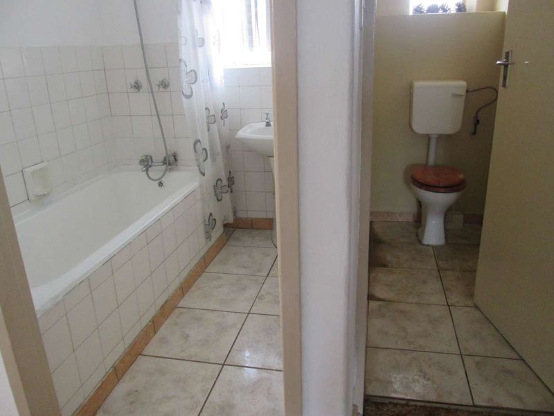 A dated bathroom featuring a separate toilet area, bathtub with shower attachment, and pedestal basin with tiled finishes throughout.