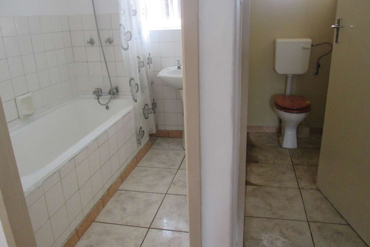 A dated bathroom featuring a separate toilet area, bathtub with shower attachment, and pedestal basin with tiled finishes throughout.