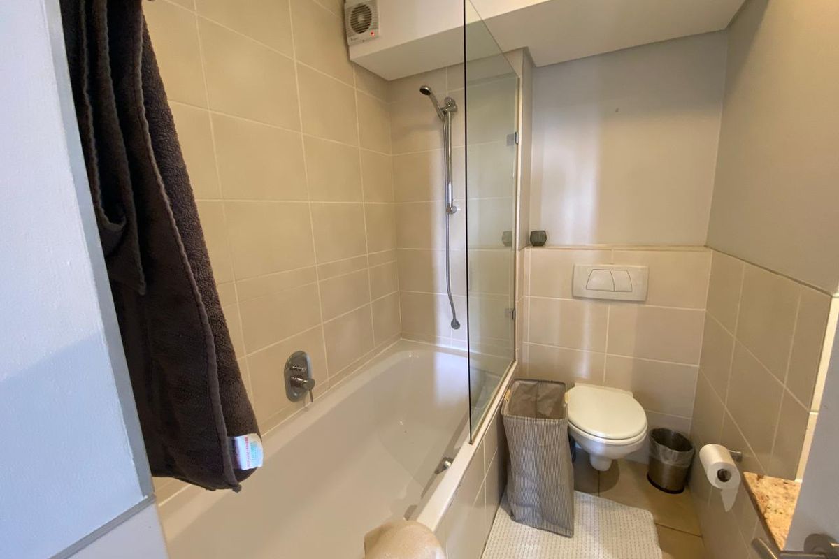 A functional bathroom featuring a bathtub with a glass shower screen, wall-hung toilet with concealed cistern, and neutral wall tiling.