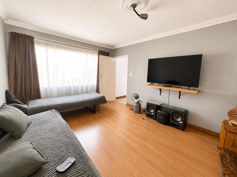 A living room featuring laminate flooring, decorative ceiling coving, and a ceiling rose, providing a functional and neutral space.