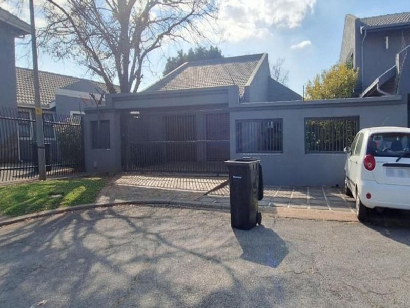 Front exterior view of the property featuring a paved driveway, secure perimeter wall, and gated entrance.