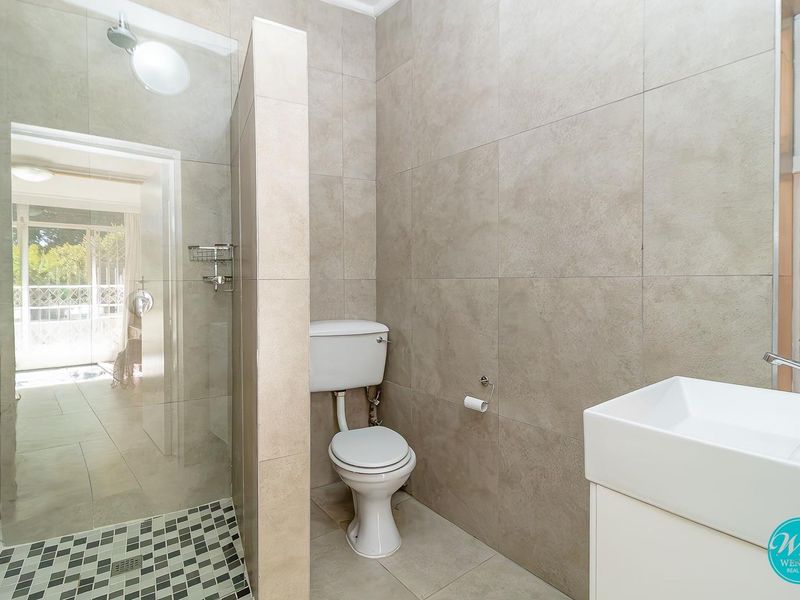 Modern bathroom featuring a walk-in shower with glass screen, contemporary vanity basin, and neutral floor-to-ceiling tiling.