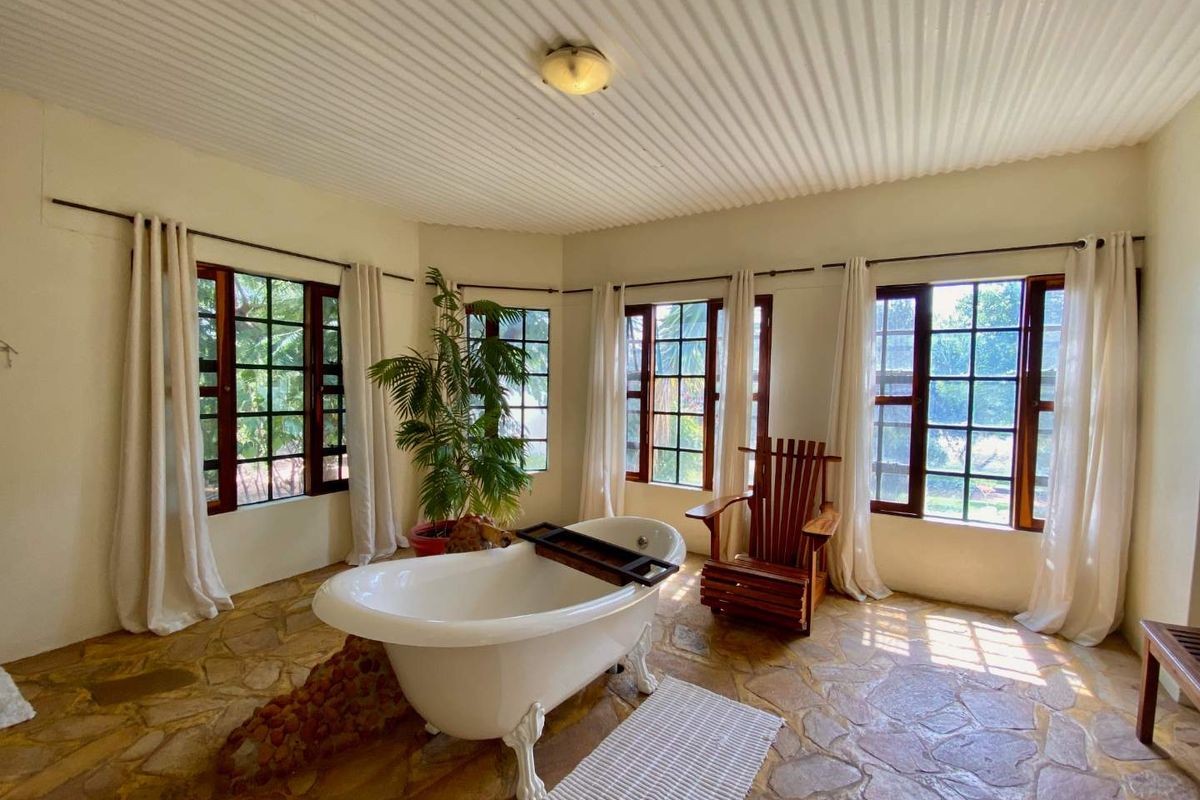 A spacious bathroom featuring a classic clawfoot bathtub, rustic stone flooring, and large windows that provide ample natural light and garden views.