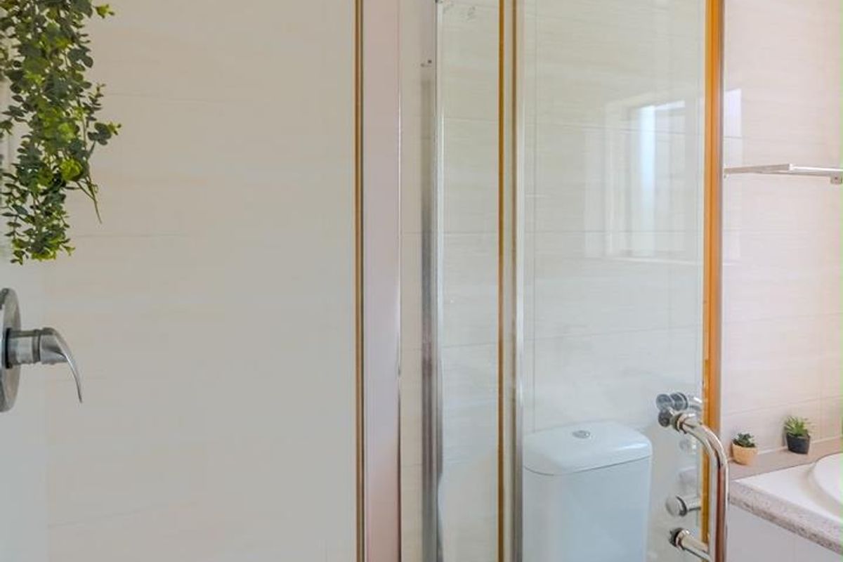 A compact bathroom featuring a glass-enclosed shower, modern toilet, and neutral wall tiling with a decorative mosaic floor pattern.