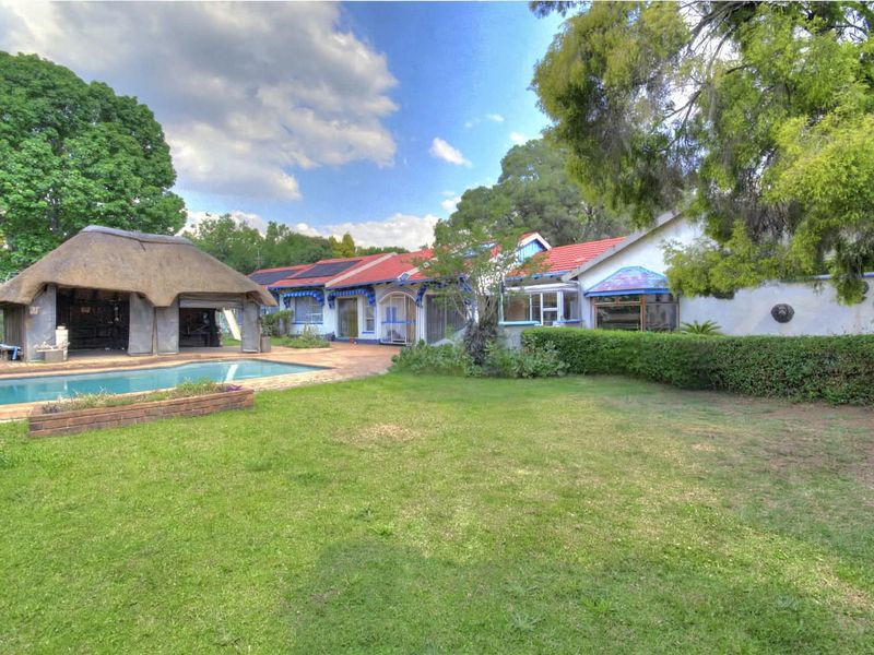 Spacious rear garden featuring a swimming pool and a traditional thatch roof lapa, set against the main house with tiled roofing and solar panels.