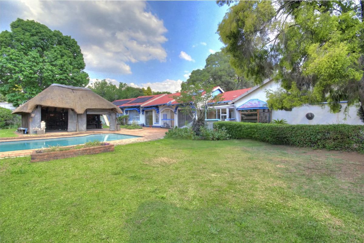 Spacious rear garden featuring a swimming pool and a traditional thatch roof lapa, set against the main house with tiled roofing and solar panels.