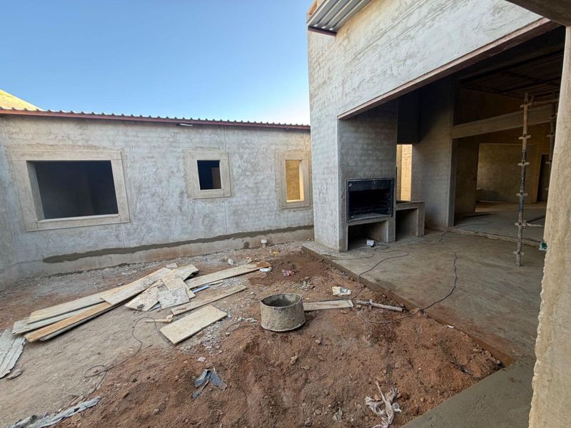Rear exterior view of a property under construction, featuring a built-in braai area and unfinished patio space awaiting final landscaping and finishes.