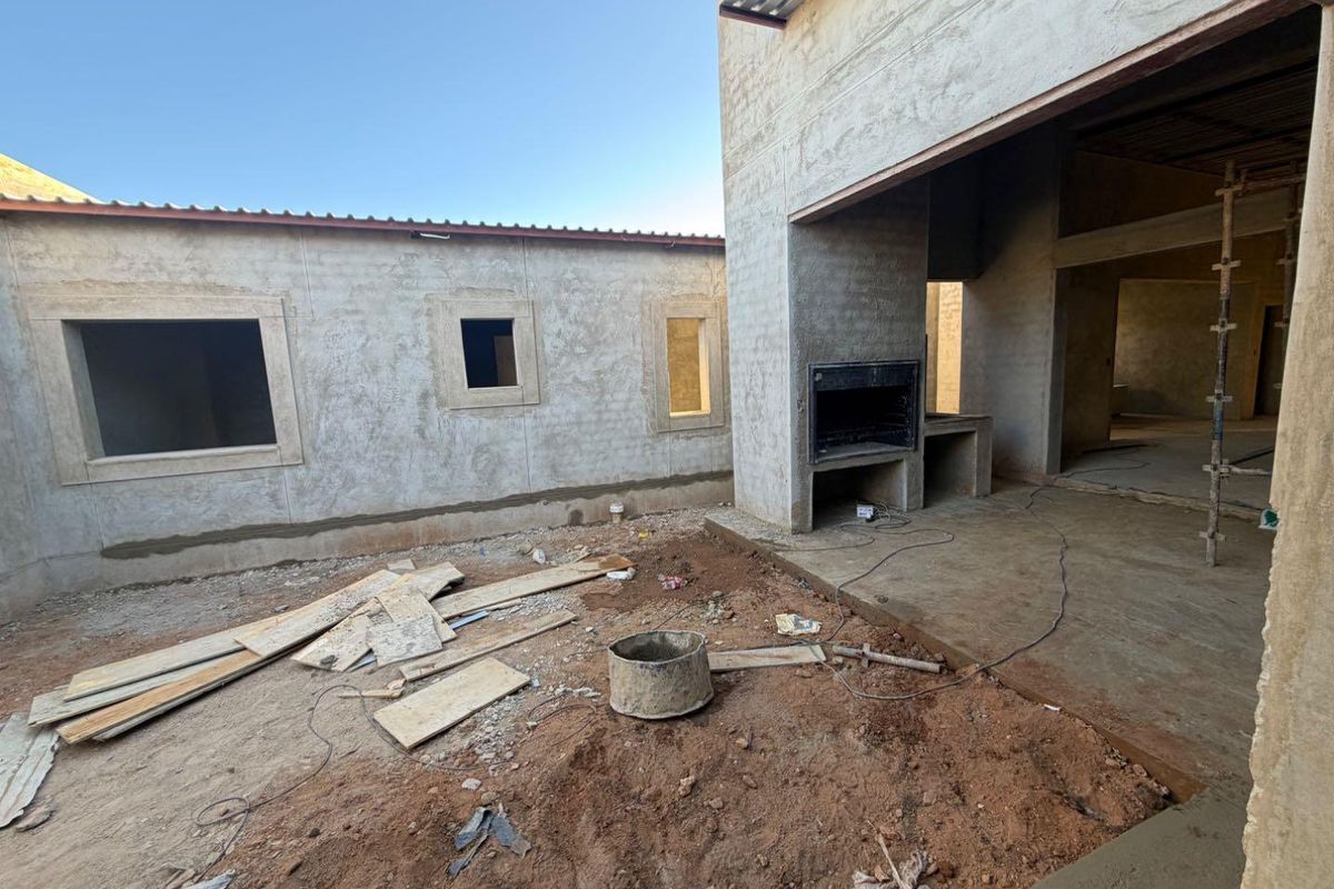 Rear exterior view of a property under construction, featuring a built-in braai area and unfinished patio space awaiting final landscaping and finishes.