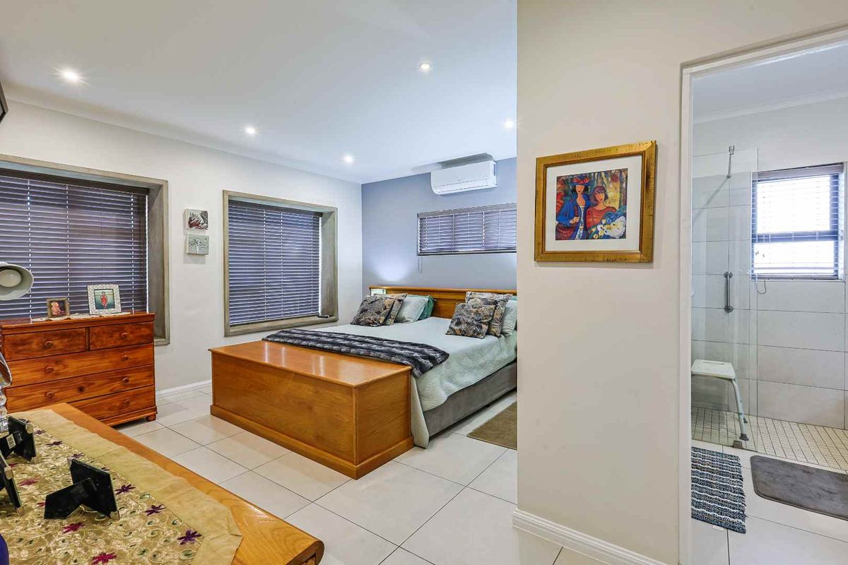 Spacious bedroom featuring tiled flooring, recessed lighting, wall-mounted air conditioning unit, and an en-suite bathroom with a walk-in shower.