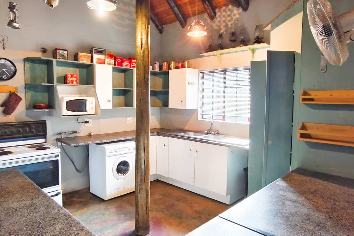 A rustic kitchen featuring built-in cabinetry, a freestanding stove, integrated laundry appliance space, and exposed timber ceiling beams.