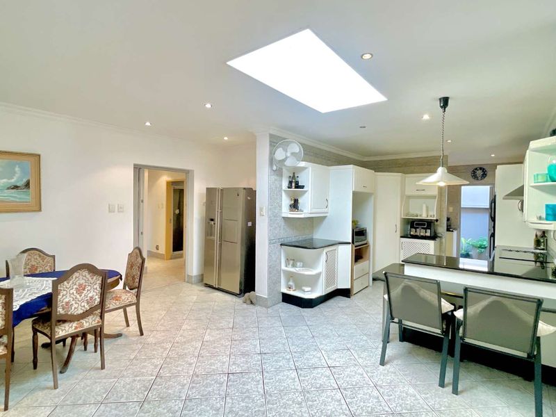 Open-plan kitchen and dining area featuring tiled flooring, built-in cabinetry with granite countertops, a breakfast bar, and a large skylight providing natural light.