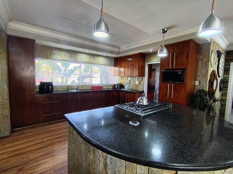 Spacious kitchen featuring dark wood cabinetry, granite countertops, a central island with a gas hob, and stone-clad accents.