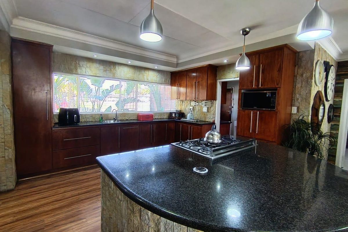 Spacious kitchen featuring dark wood cabinetry, granite countertops, a central island with a gas hob, and stone-clad accents.