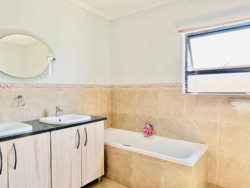 A functional bathroom featuring a dual vanity with granite countertop, tiled bathtub surround, and neutral wall tiling.