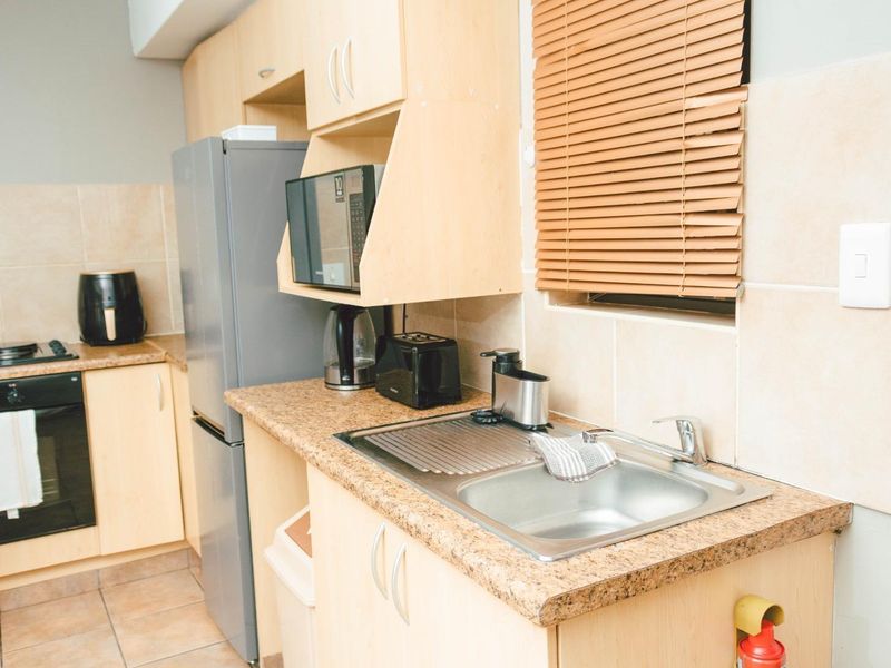 A functional kitchen featuring light wood-look cabinetry, granite-style laminate countertops, a stainless steel sink, and built-in cooking appliances with tiled splashbacks.