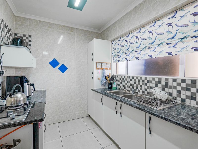 A functional kitchen featuring granite countertops, a double basin sink, gas hob, and ample built-in cabinetry with tiled finishes throughout.