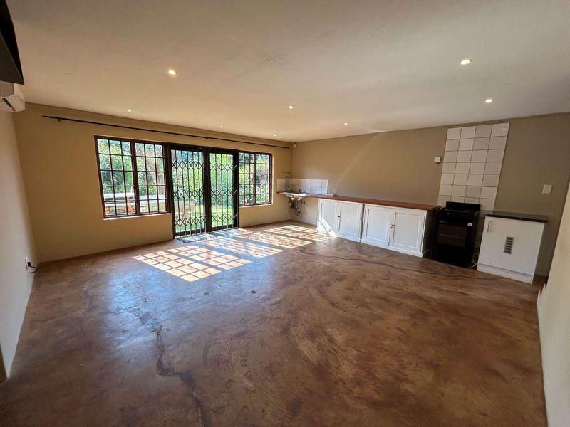 Spacious open-plan living and kitchen area featuring polished concrete floors, built-in cabinetry, and direct access to the garden through security-gated doors.