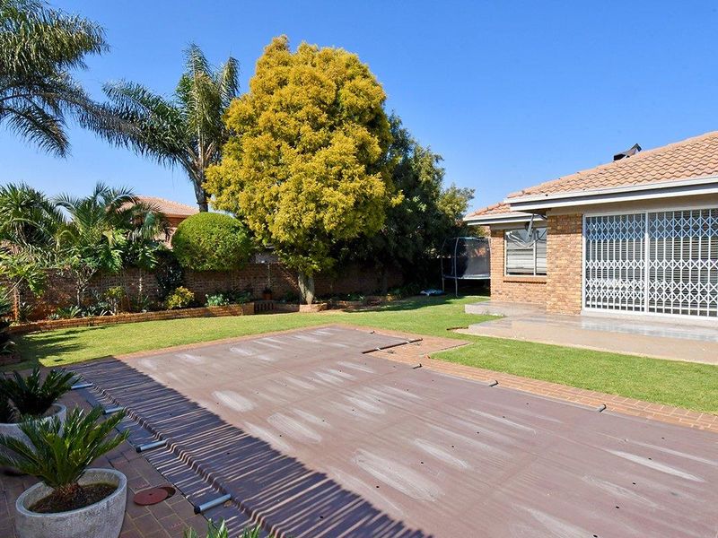 A well-maintained rear garden featuring a covered swimming pool, paved patio area, and established landscaping with a brick boundary wall.