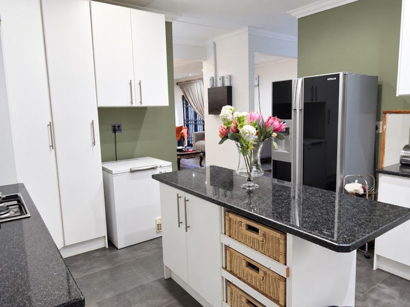 A functional kitchen featuring granite countertops, a central island with storage, and white cabinetry, with an open-plan flow into the adjacent living area.