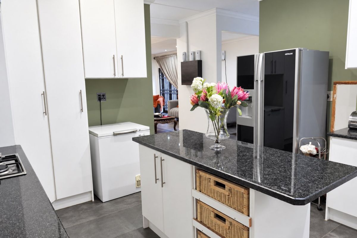 A functional kitchen featuring granite countertops, a central island with storage, and white cabinetry, with an open-plan flow into the adjacent living area.