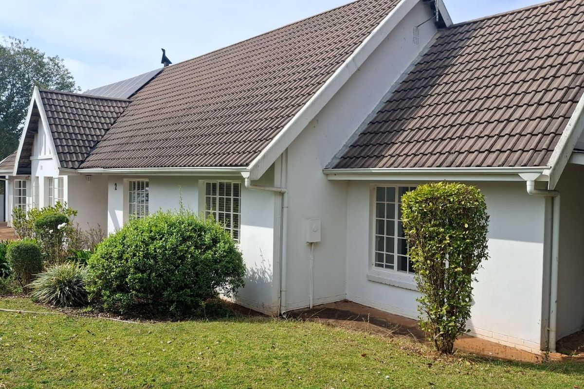 A view of the rear exterior of the house featuring a tiled roof, white facade, and grid windows set against a landscaped garden.